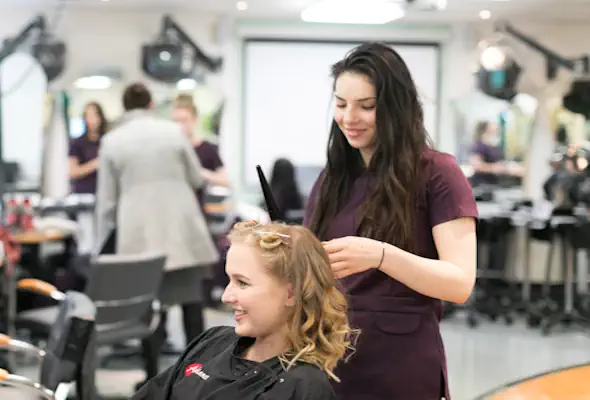 A student styling a model's hair with a curling iron.