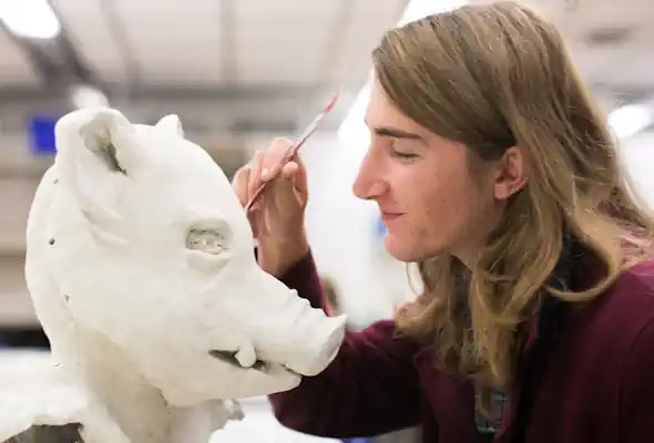 A student sculpts a boar's face with a tool.
