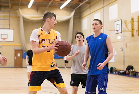 Three students play basketball in the sports hall.