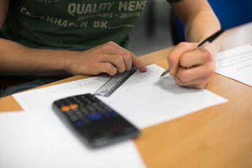 a student using a ruler, pencil and paper with a calculator