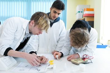 three students in lab coats in class