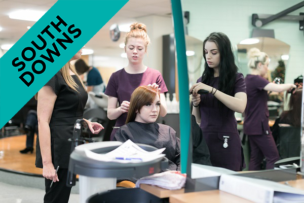 a student working on a client's hair in the college salon, with their lecturer