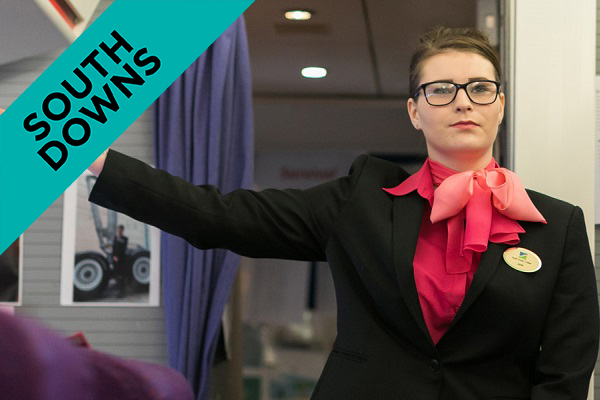 An air cabin crew student pointing towards emergency exit on a plane