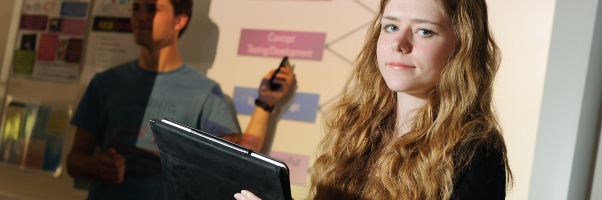 a student holding a tablet, looking in to the camera
