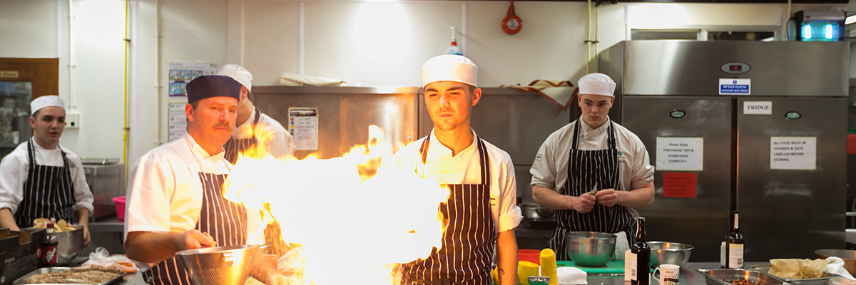 students cooking with fire in college kitchen