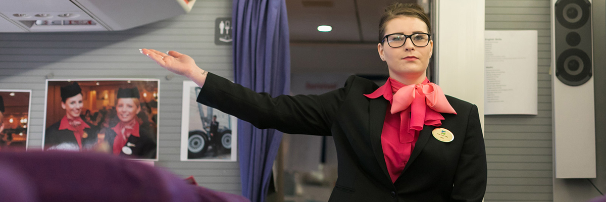 An air cabin crew student pointing towards emergency exit on a plane