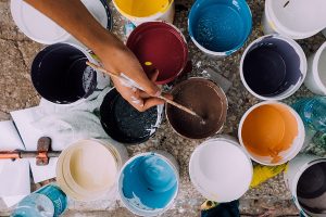 pots of different coloured paint on the floor with someone dipping their paintbrush in one