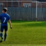 boy in football kit on field in front of goal