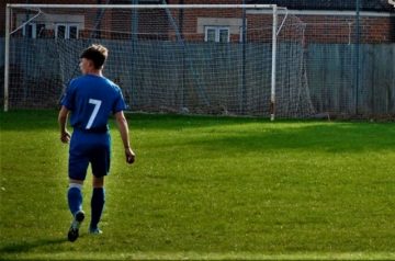 boy in football kit on field in front of goal