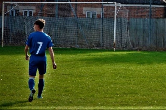 boy in football kit on field in front of goal