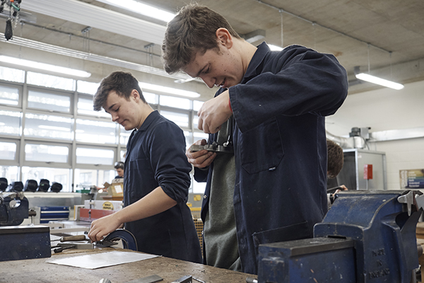 two students in overalls in college workshop