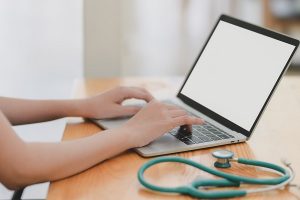 a nurse typing on a laptop with a stethoscope next to them