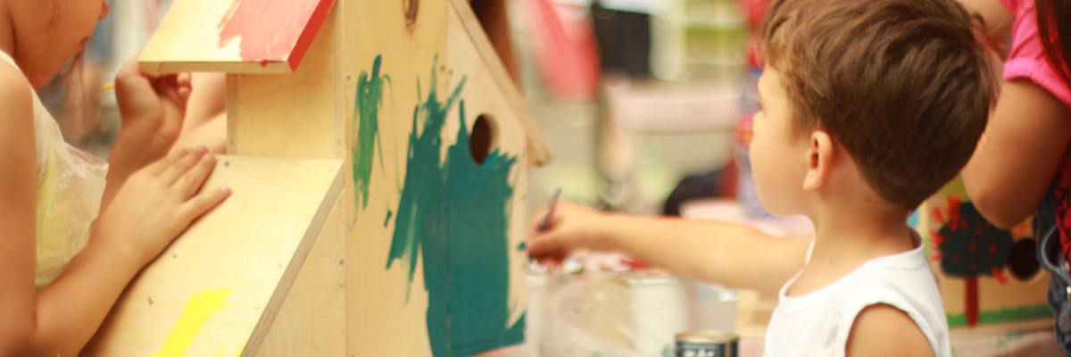 young child painting a wooden house