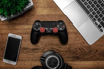 a ps4 controller, headphones, laptop and iphone on a desk