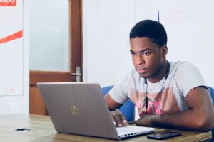 a male sitting in front of a laptop with a mobile by his side