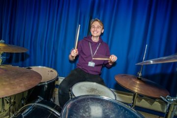 smiley male student playing a drum kit