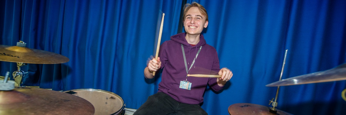 smiley male student playing a drum kit