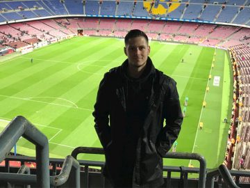 Young man standing in front of Premier league football pitch