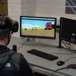 student with a headset on in front of two computer monitors