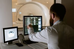 a man in a lab coat pointing at some MRI scans on a computer screen