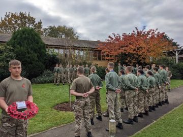 Students in armed forces uniform gather around the memorial tree