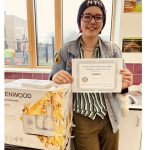 Alana holds her first place certificate and stands next to her food processor prize