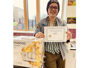Alana holds her first place certificate and stands next to her food processor prize