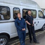 Alex and Josh stood against a minibus in their overalls