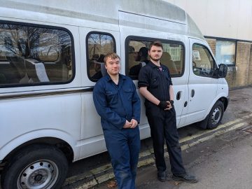 Alex and Josh stood against a minibus in their overalls