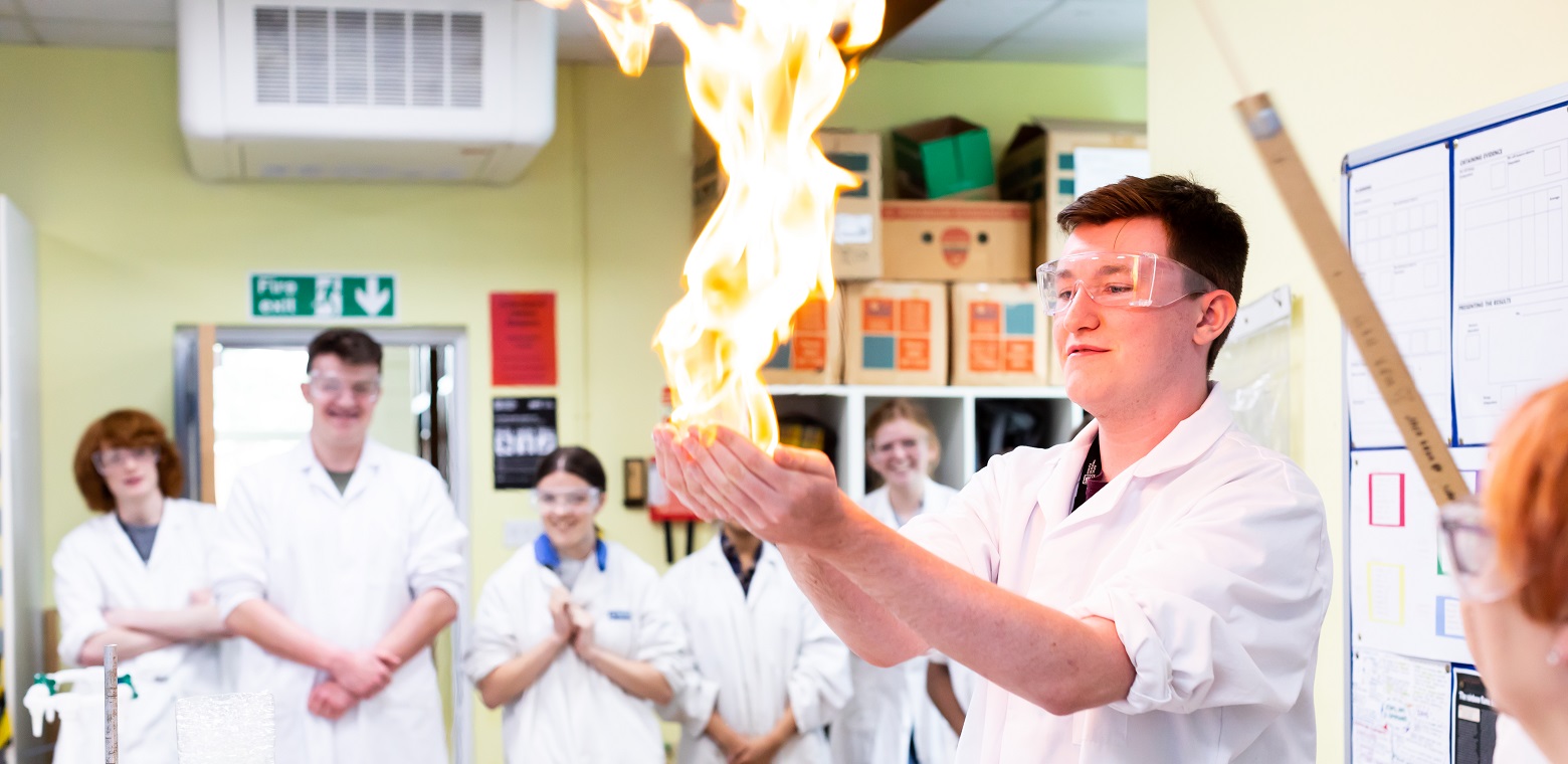 students in lab coats watching a fellow student with fire in his hands