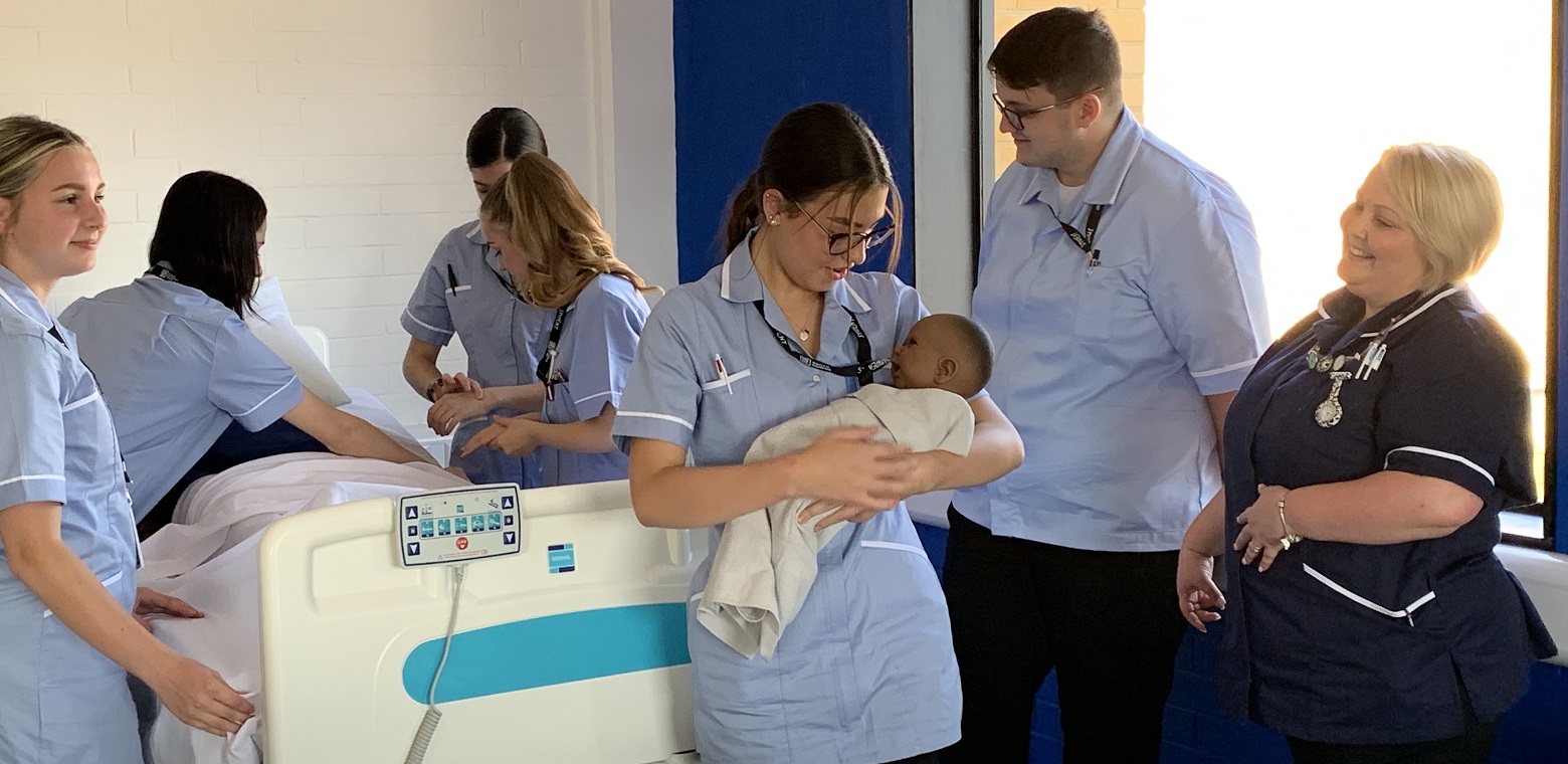 nursing t level students in their uniforms with one holding a simulator baby