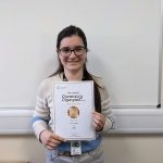 Lucy smiling with her gold award certificate