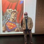 Artist Ian Churchill poses next to an artwork of Superman