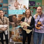 Three smiling students holding baby dolls