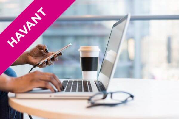 a woman typing at a laptop whilst using her mobile phone with a coffee