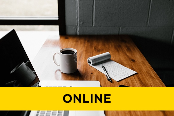 A coffee cup, notepad and laptop on a desk.