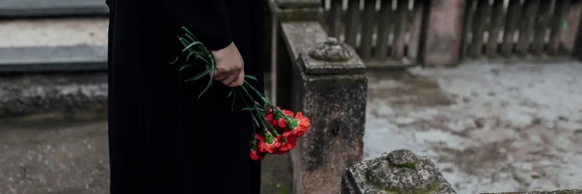 Closeup side profile of someone holding red flowers in a graveyard.