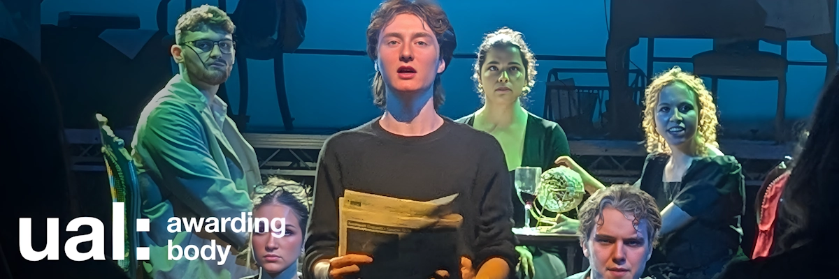 A student lit with a spotlight reads from a newspaper while other students sit behind in eerie green light as part of a stage performance.