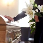 An image of someone holding lilies next to a coffin.
