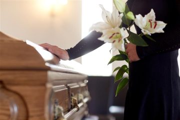 An image of someone holding lilies next to a coffin.