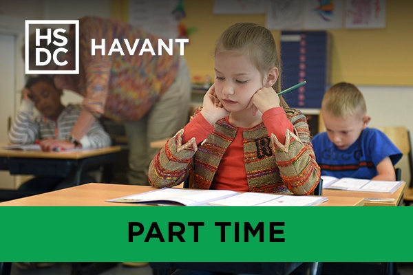 a child in a classroom with a teacher helping another child in the background.