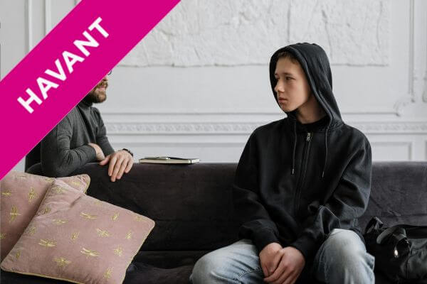 A young person on a sofa, being spoken to by a mental health professional.