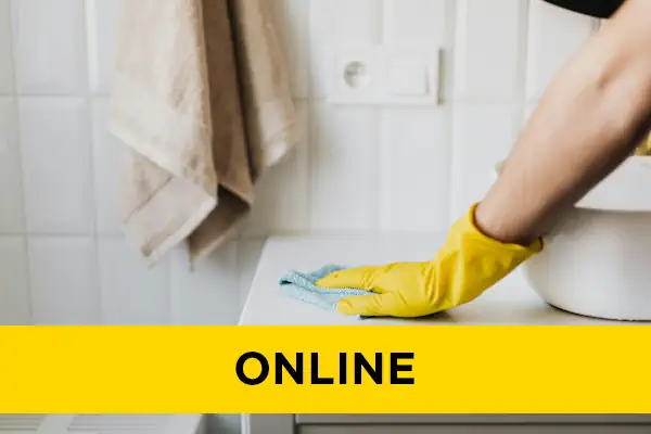 Closeup of a yellow gloved hand cleaning a white bathroom counter with a cloth.