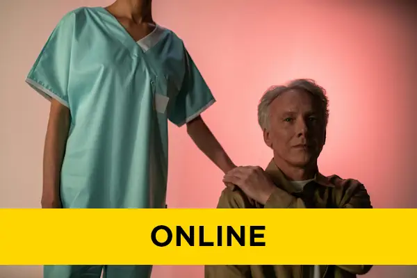 An older gentleman sits, grasping a nurse's hand on his shoulder.