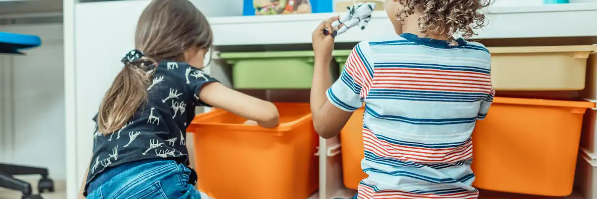 Behind shot of two children playing with toys from orange boxes.