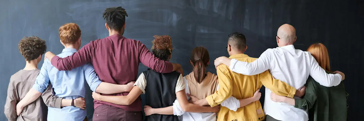 A group of individuals stood with their backs to the camera, arms around eachother.