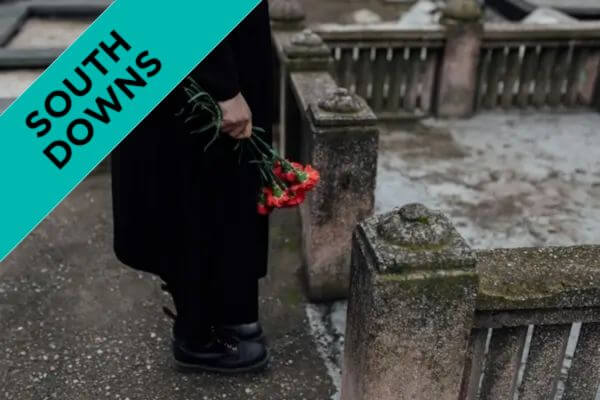 Closeup side profile of someone holding red flowers in a graveyard.