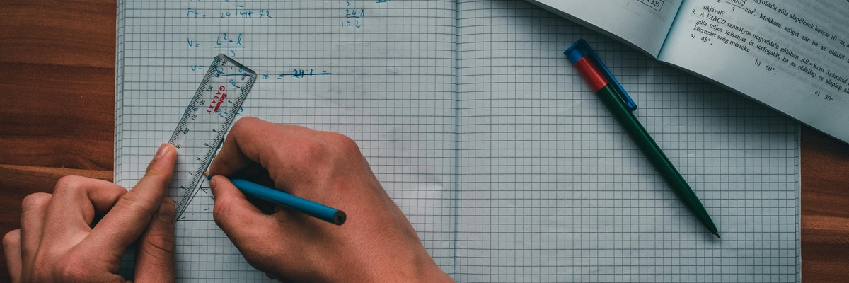 A person using a ruler to do maths work with a textbook beside them.