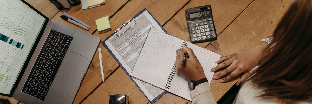 Someone filling in a work planner on a cluttered office desk.