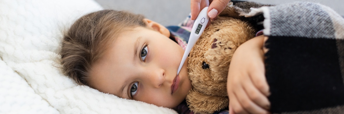 A sick child in bed with a teddy bear and thermometer.